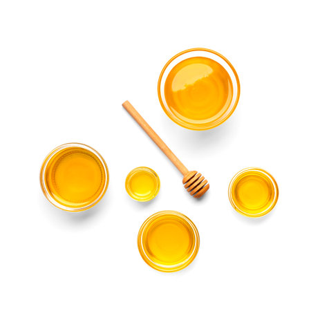 Creative composition of honey in glass bowls of different sizes and a wooden dipper on a white background top view. Organic honey and honey spoon isolated.の写真素材