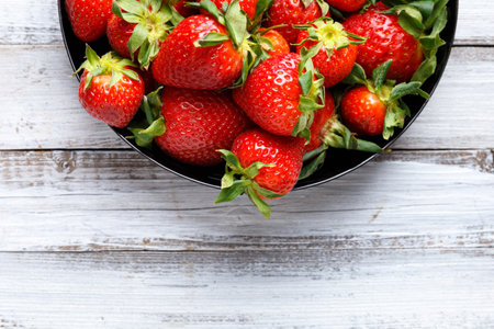 Fresh organic strawberries in a black round plate on a light wooden background, top view, with space for text.の写真素材