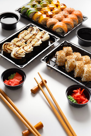 Set of sushi rolls in plastic takeaway packages with soy sauce, ginger, wasabi and chinese chopsticks on a white background. Delivery of sushi in a plastic containerの写真素材