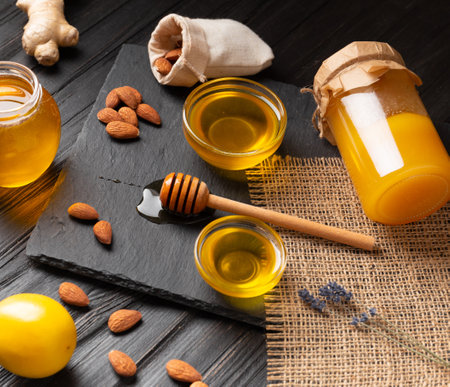 Honey in jars, dipper, lemon, ginger on a black stone plate on a wooden background. The concept of organic bee products.の写真素材