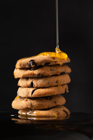 Honey pours on homemade cookies with pieces of chocolate on a dark background close-up. A composition of craft cookies and pouring honey.の写真素材