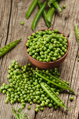 Fresh organic green peas in closed and open pods, scattered pea seeds, shelled green peas in a clay bowl on an aged wooden background. vegetable proteins.の写真素材
