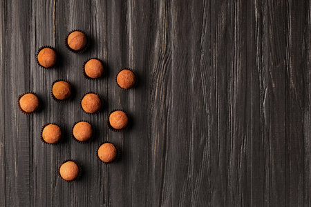 A lot of chocolate truffles in individual paper packages on a dark wooden background, top view, copy space. Round handmade sweets sprinkled with cocoa powder.の写真素材