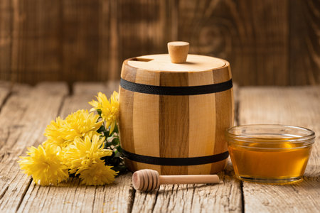 Honey in a wooden barrel and a transparent bowl, a wooden dipper and yellow flowers on a wooden background.の写真素材