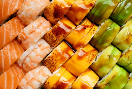A set of bright multi-colored sushi rolls with shrimp, salmon, eel, avocado, cheese, poured with sauce, top view, close-up.の写真素材