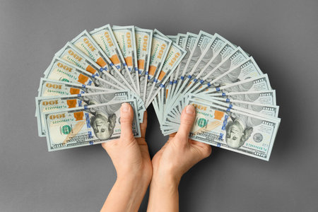 A lot of bills of 100 dollars in hands are folded in a fan on a gray background top view. Currency, banknotes in female hands. The concept of success, business, wealth.の写真素材