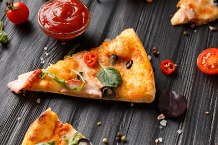 Pizza slices with jerky, olives, cheese and herbs are laid out on a dark wooden background, fresh cherry tomatoes, sauces and seasonings for pizza, top view. Italian food.の写真素材