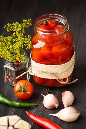 Canned cherry tomatoes in an open jar, garlic, hot peppers, spices and herbs on a dark textural background, close-up. Ingredients for Preserving Tomatoes.の写真素材