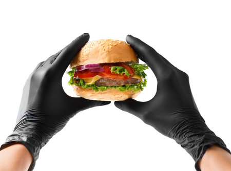 Hands in black gloves hold a juicy, appetizing beef burger on a white background. Hamburger in hands isolated. Banner, fast food advertising.の写真素材