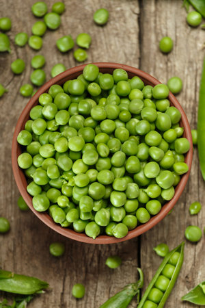 Fresh organic green peas in closed and open pods, scattered pea seeds, shelled green peas in a clay bowl on an aged wooden background, top view. vegetable proteins.の写真素材