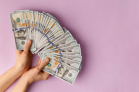 A lot of bills of 100 dollars in hands are folded in a fan on a pink background. Currency, banknotes in female hands. The concept of success, business, wealth.の写真素材