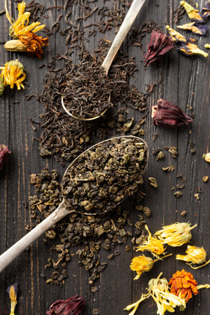 Composition of dry black and green tea in vintage spoons, dry flowers tea on a dark wooden background top view close-up. Different types of dry tea on a dark background.の写真素材