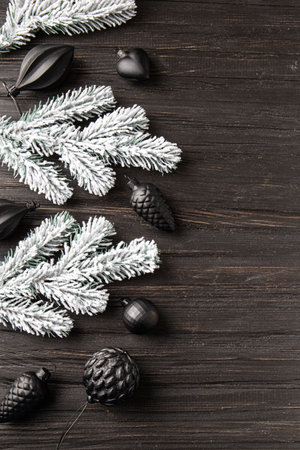 New Year's decor on a dark background with a place for text. Fir branch in the snow and Christmas decorations in black on a wooden background.の写真素材