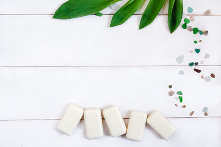 Pieces of white toilet soap , a scattering of colorful pebbles and green fresh leaves on a white...
