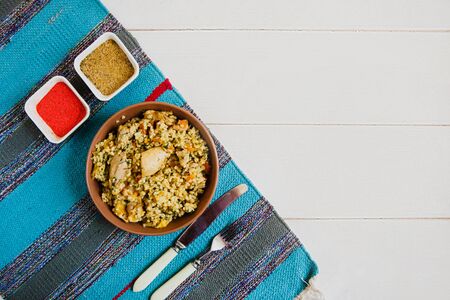 The national dish is Uzbek pilaf with chicken on the blue striped mat lying on a white background. There are also Cutlery and condiments nearby. Flat layout with space for textの写真素材