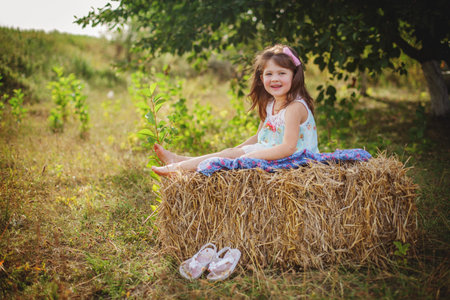 portrait of a smiling girl with dark hair in a lilac jumpsuit, holding on to a tree branch with one hand in summerの写真素材