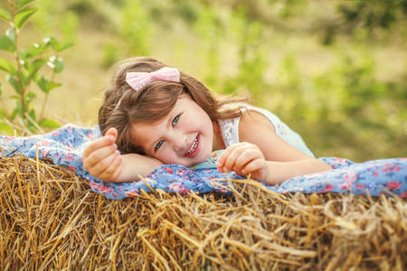 portrait of a smiling girl with dark hair in a lilac jumpsuit, holding on to a tree branch with one hand in summerの写真素材