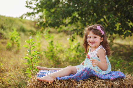 portrait of a smiling girl with dark hair in a lilac jumpsuit, holding on to a tree branch with one hand in summerの写真素材