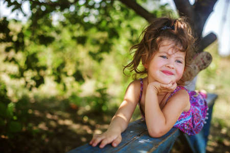 portrait of a smiling girl with dark hair in a lilac jumpsuit, holding on to a tree branch with one hand in summerの写真素材