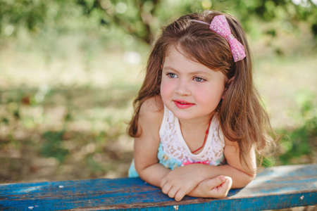 portrait of a smiling girl with dark hair in a lilac jumpsuit, holding on to a tree branch with one hand in summerの写真素材