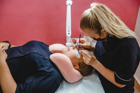 Eyelash Extension process. Master in black uniform does procedure in the beauty salon.の写真素材