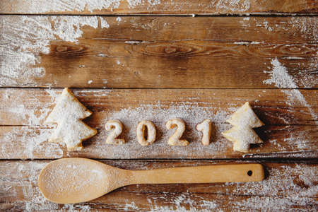 Bakery Flat lay with cookies in form of Christmas trees and numbers 2021, flour, wooden spoon on the wooden table. Copyspace.の写真素材
