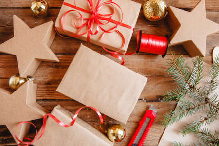 Wrapping Christmas gifts in craft paper and red ribbon. There are stationery knife, gold balls, ribbon and a fir branch. Flat layoutの写真素材