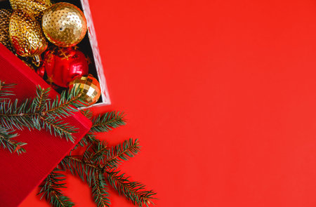 Open gift box with red and golden Christmas balls on a red background. Near the spruce branch. High...