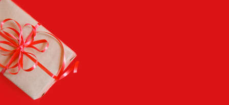 Flatlay from Christmas gifts in craft paper, red ribbon and a fir branch on red background. High quality photoの写真素材