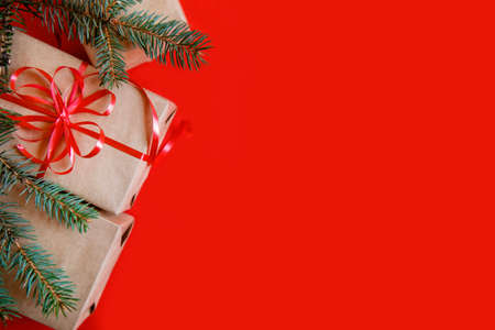 Flatlay from Christmas gifts in craft paper, red ribbon and a fir branch on red background. High quality photoの写真素材