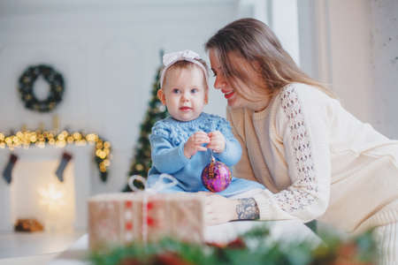 Mother with daughter in knitted clothes in a bright room at a table. Christmas atmosphere - fireplace, gifts, bokeh.の写真素材
