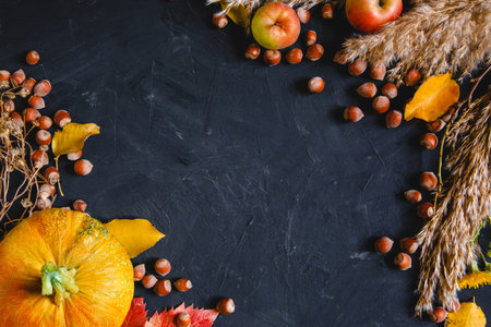 Autumn frame on a dark background of pumpkins, apples, nuts and dried flowers. Flat layout with...