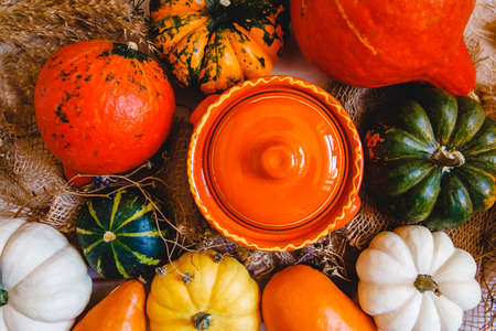 An orange clay pot and lots of colorful pumpkins on a burlap on a table. Flat layoutの写真素材