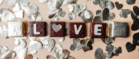 The word love is made of wooden letters on square chocolates. Around cut out hearts from foil. Valentine's day flat lay. High quality photoの写真素材