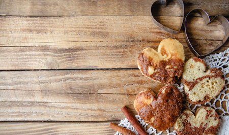 Heart-shaped buns, openwork tablecloth, baking pans and cinnamon on a wooden table. Flat lay with copy spaceの写真素材