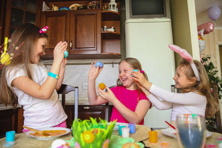 three girls with painted Easter eggs in their hands are laughing and fooling around at home in the kitchenの写真素材