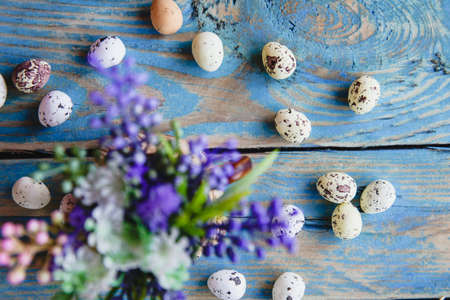 Bouquet of spring purple flowers and a scattering of quail eggs on an old, worn blue table. Vintage flat layoutの写真素材