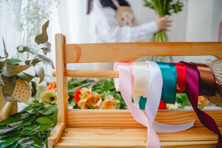 A wooden stand with colorful ribbons and twine on a florists table littered with flowersの写真素材