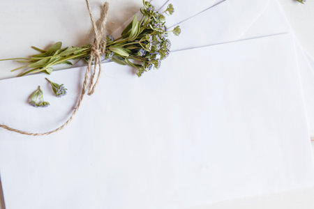 A white blank envelopes with a small bouquet of wildflowers tied with twine on a white wooden...