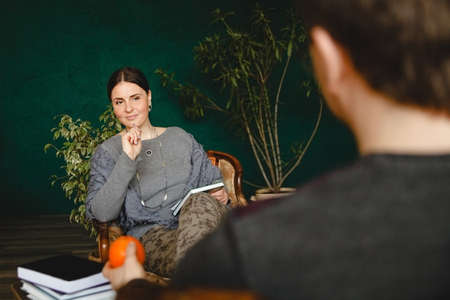 A brunette woman psychologist of European appearance conducts a patient's appointment in her office. She sits across from him and listens intently. High quality photoの写真素材
