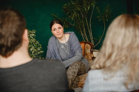 A young brunette woman psychologist sits opposite a married couple during a appointment in her office and listens attentively to them. High quality photoの写真素材