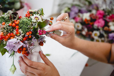 A florist makes a bouquet of different flowers and rose hips in a white vase at a white table in his workshopの写真素材