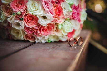 wedding rings on the wooden floor near the bouquet of rosesの写真素材
