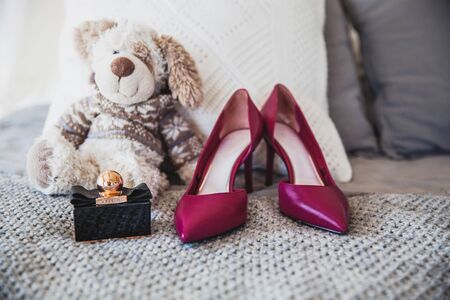 red high-heeled shoes, perfume and soft toy on the bedの写真素材