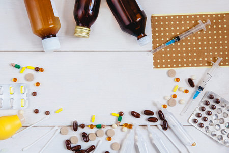 Medicines on a white wooden background - scattered colored tablets, ampoules, syringes, patch,...