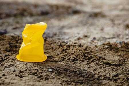 One yellow crumpled plastic Cup standing on the ground. Global concept of environmental disasterの写真素材