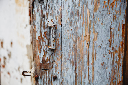 Old shebby wooden door with remnants of old paint. A handle is bolted to the door.