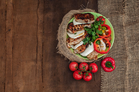 a plate of cooked meat, cheese and vegetables on a wooden table. Near tablecloth from burlap fabricの写真素材