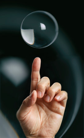 finger pointing a transparent crystal ball with black background.