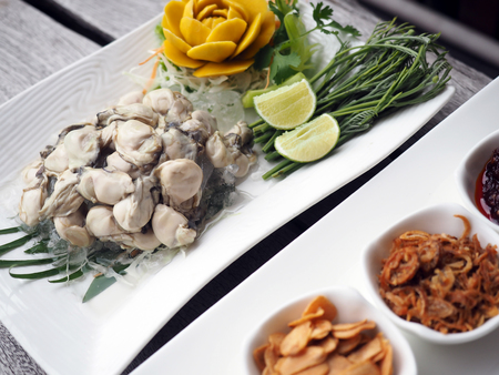 Thai style fresh oyster serve with herbal condiment, white dish on wooden background.の写真素材